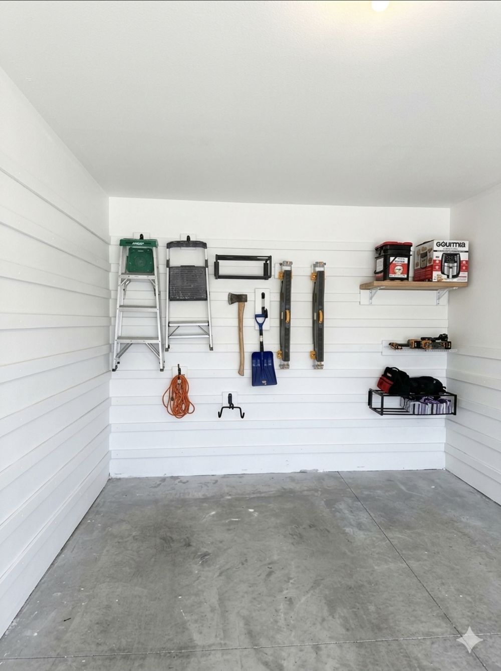 Empty garage bay with a white cleat wall, shelf and tool holders ready for gear