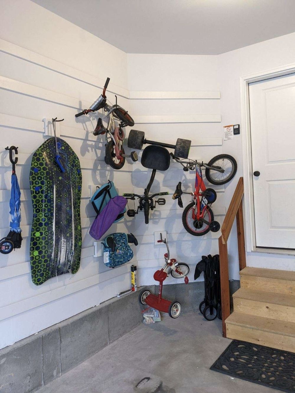 Corner of a garage with kids bikes, a boogie board and sleds hung on the cleat wall