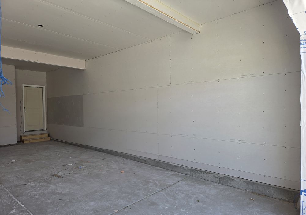 Unfinished garage with bare drywall, no storage, boards on the floor